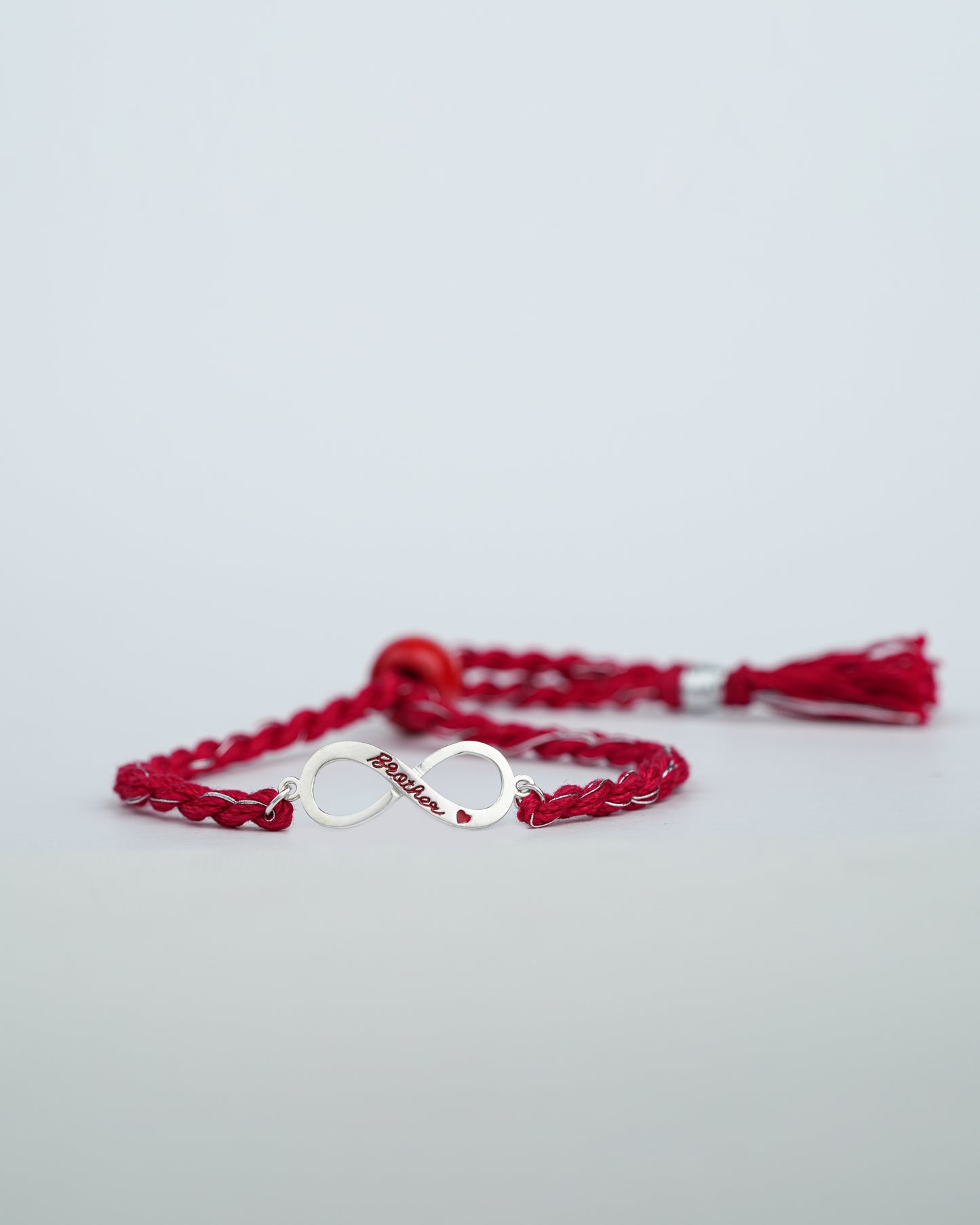 Silver infinity charm reading Brother in red enamel on a braided red rakhi