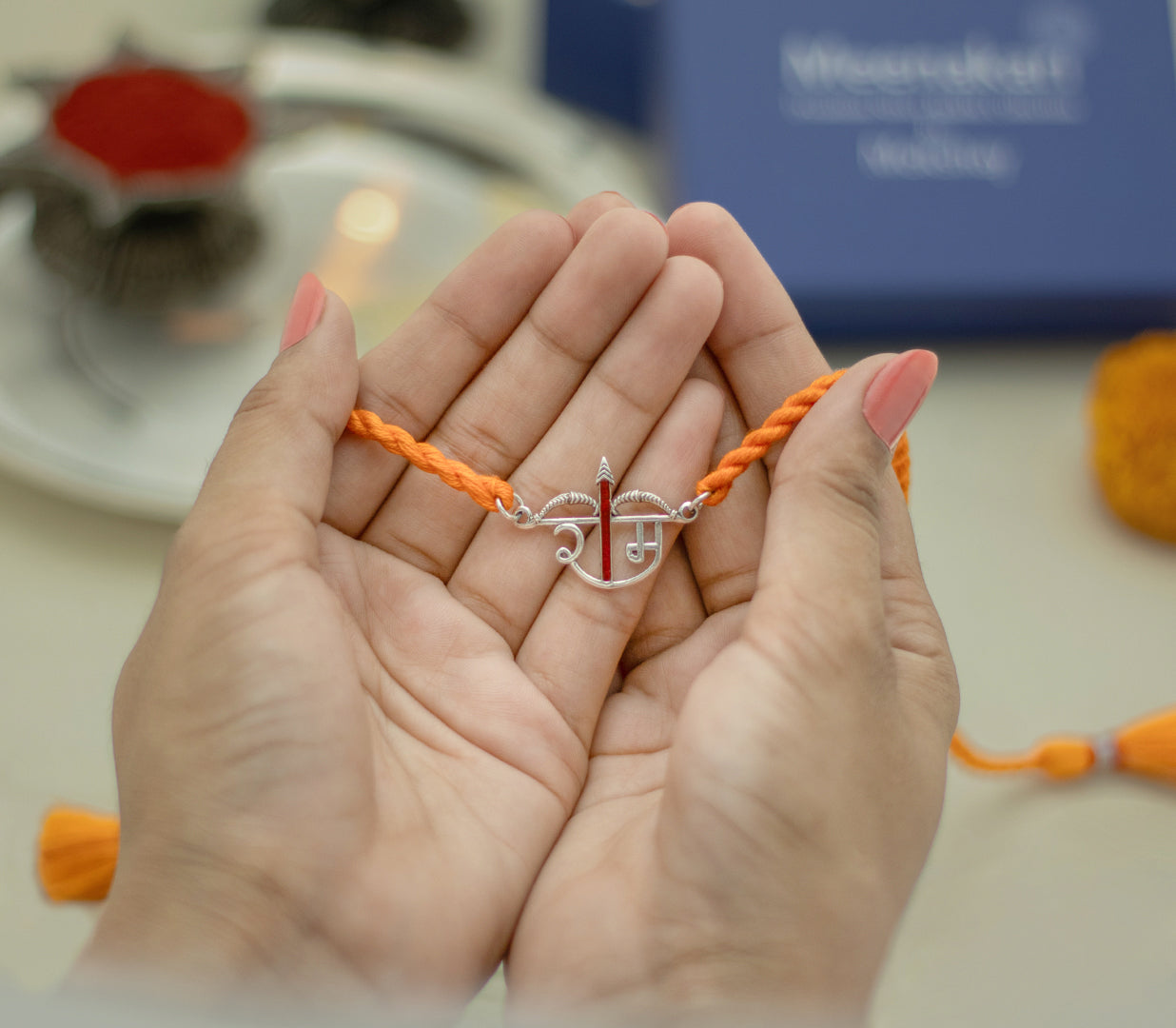 Hands holding the Ram Dhanush rakhi beside a Meenakari box