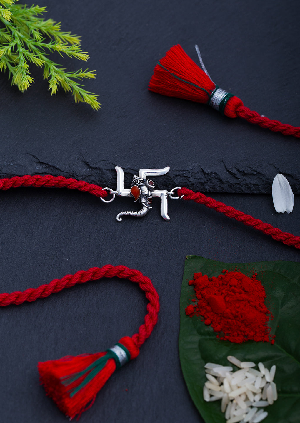 Swastik Ganesh rakhi on a dark surface with a tassel and foliage