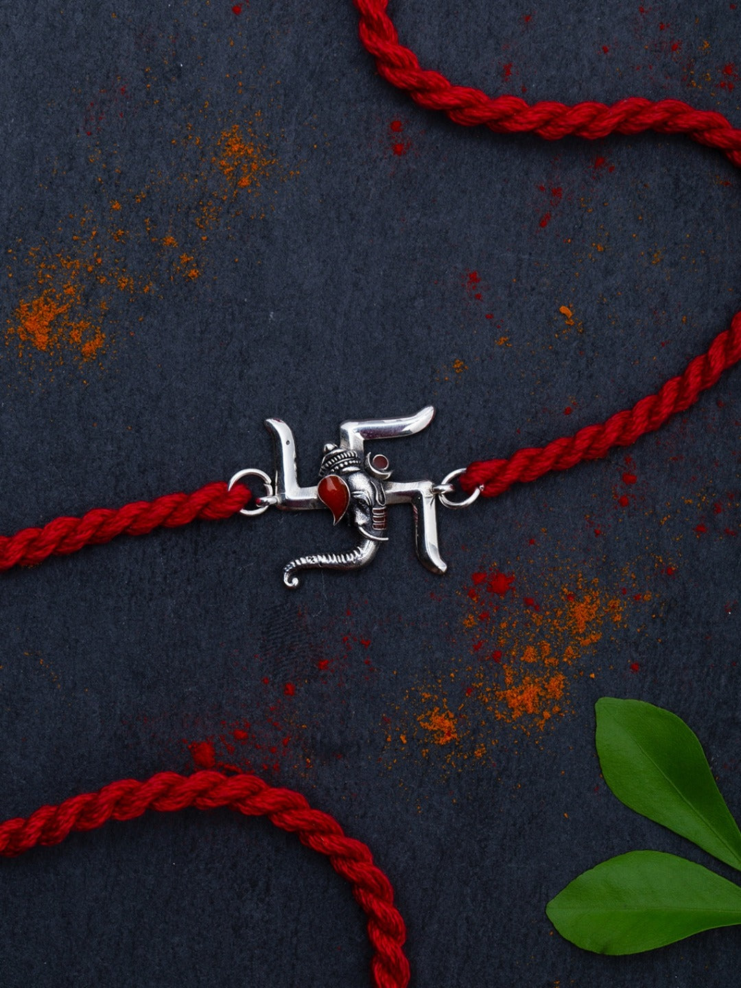 Close-up of the silver swastik charm on red thread with turmeric