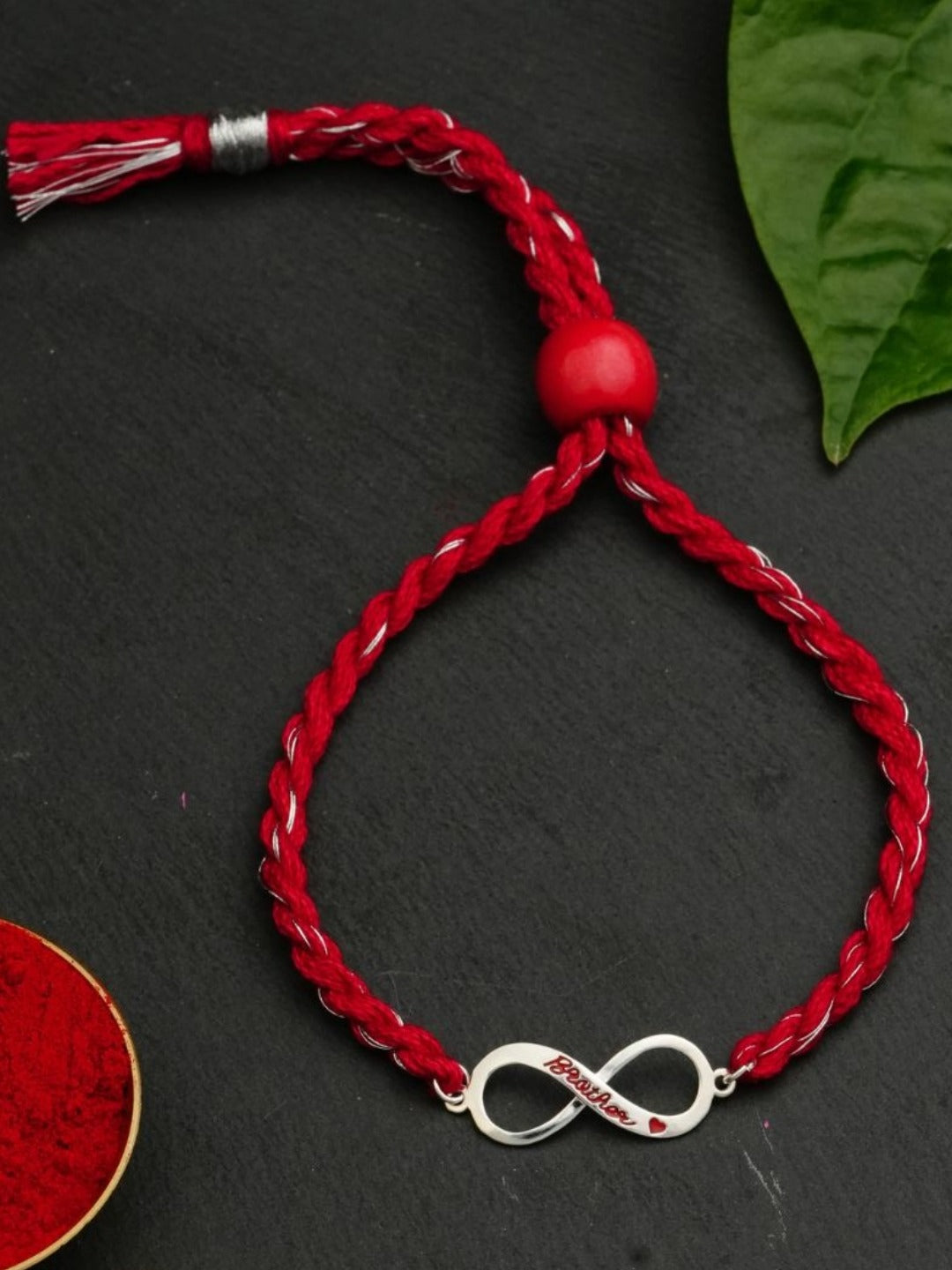 Infinity charm rakhi on a dark surface with a green leaf