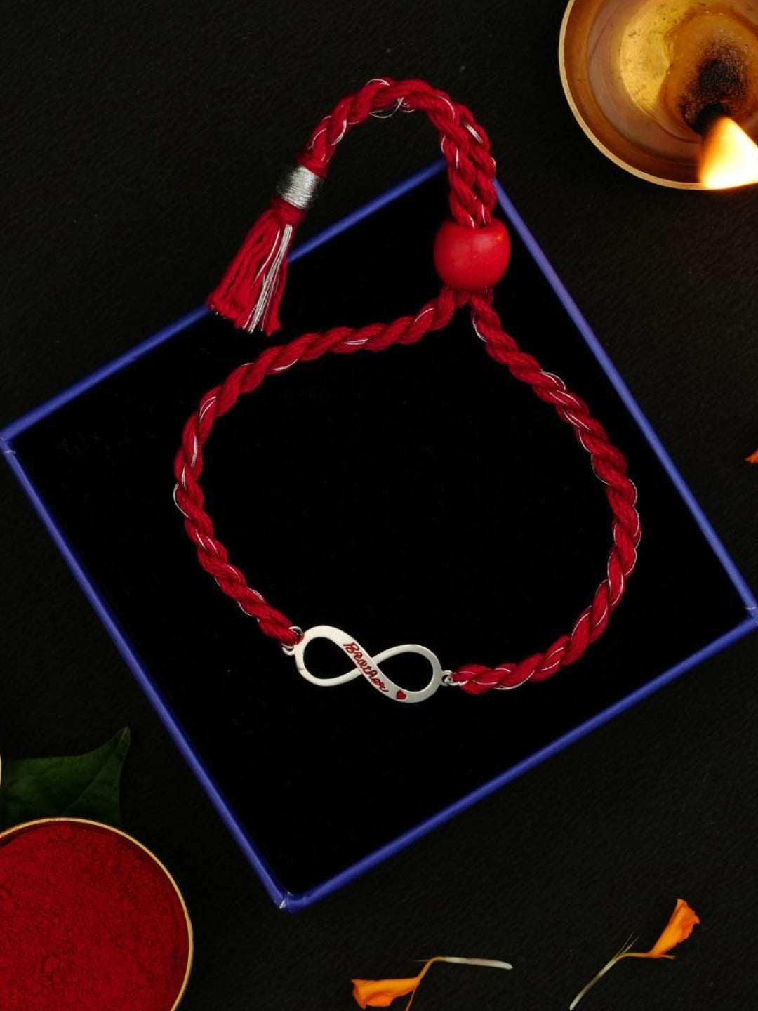 Infinity charm rakhi on a gift box beside a lit diya