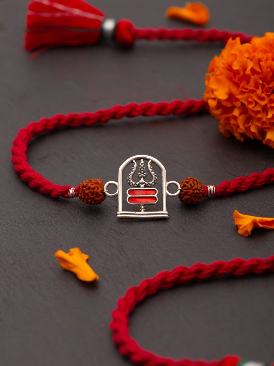 Shivalinga trishul rakhi on a dark surface with marigold petals